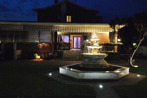 A building with a traditional architectural style, a well-lit entrance, and a fountain in the foreground. - Albergo Aurora (Castenaso)