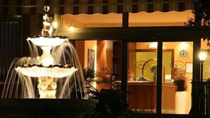 A fountain in front of a building with a reception desk visible through the glass doors. - Albergo Aurora (Castenaso)