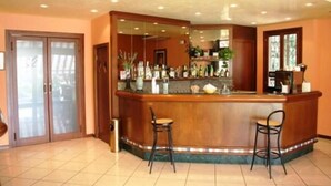 A bar area with two stools, a counter with various bottles, and a mirror above. - Albergo Aurora (Castenaso)