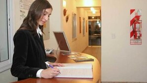 A person writing at a desk with a laptop and a notebook.