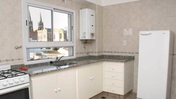 A kitchen with a gas stove, a white refrigerator, a window with a view of a building, and a water heater.