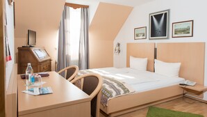 A hotel room with a bed, desk, chair, and a small table with a bottle and a magazine. - Hotel Am Friedrichsbad (Baden-Baden)