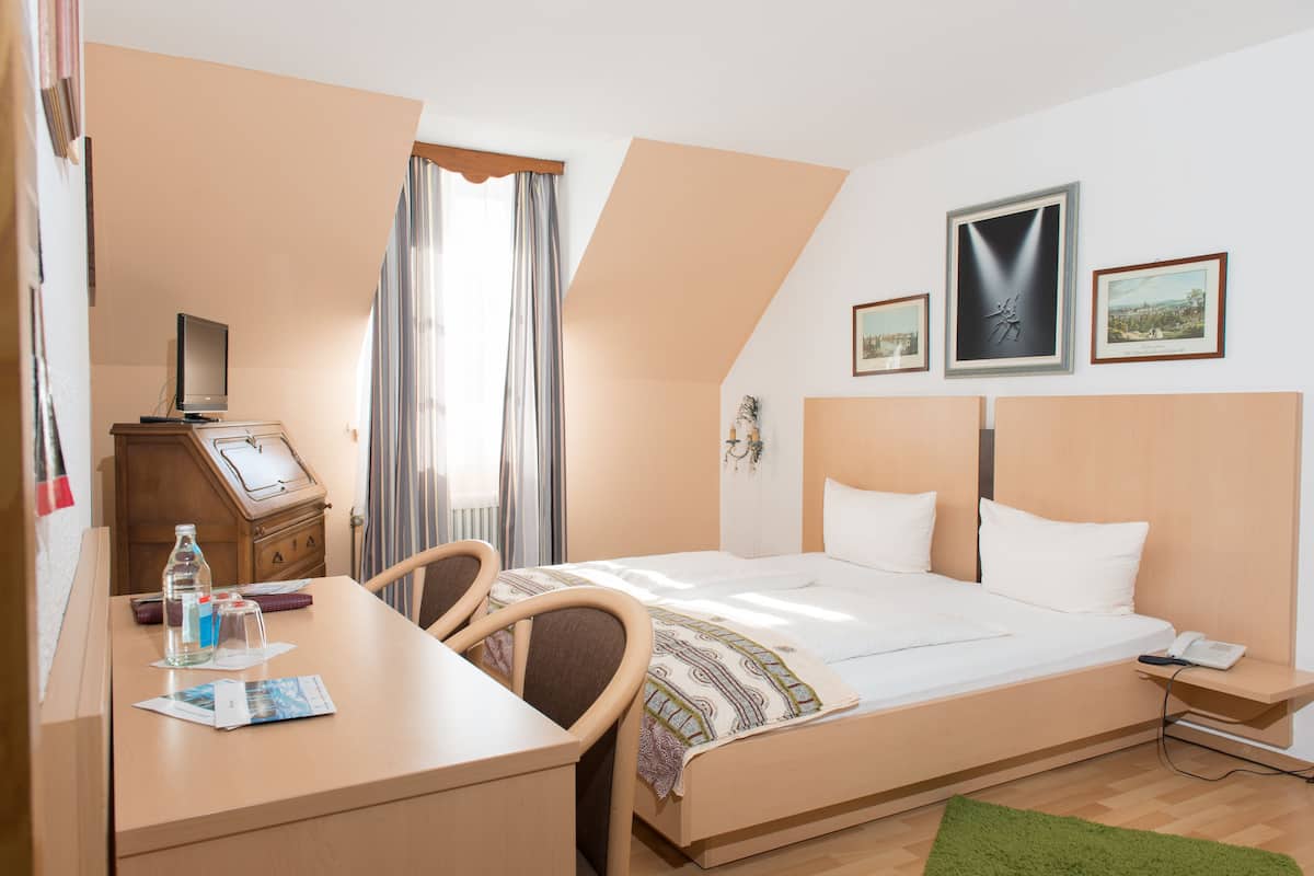 Ein Hotelzimmer mit Bett, Schreibtisch, Stuhl und einem kleinen Tisch mit Flasche und Zeitschrift.