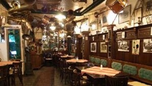 A restaurant interior with wooden tables and chairs, a patterned carpet, and wall-mounted lights. - Hotel Am Friedrichsbad (Baden-Baden)