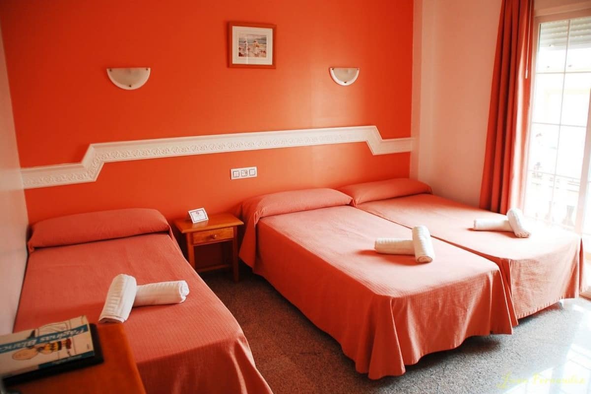A hotel room with two beds, a small table, a nightstand, and a window with curtains.