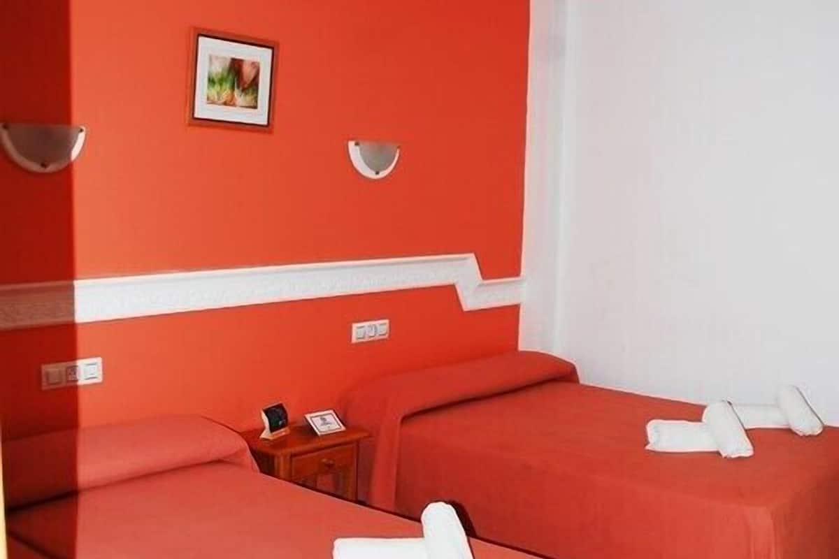 A hotel room with two beds, each with a white pillow and a small bedside table.