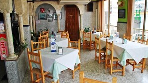 A restaurant with multiple tables and chairs, a wooden door, and framed pictures on the wall. - Mary Tere (Salobreña)