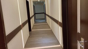 A hotel hallway with a wooden floor, white walls, and a wooden door on the right. - Hotel Oyten am Markt (Oyten)