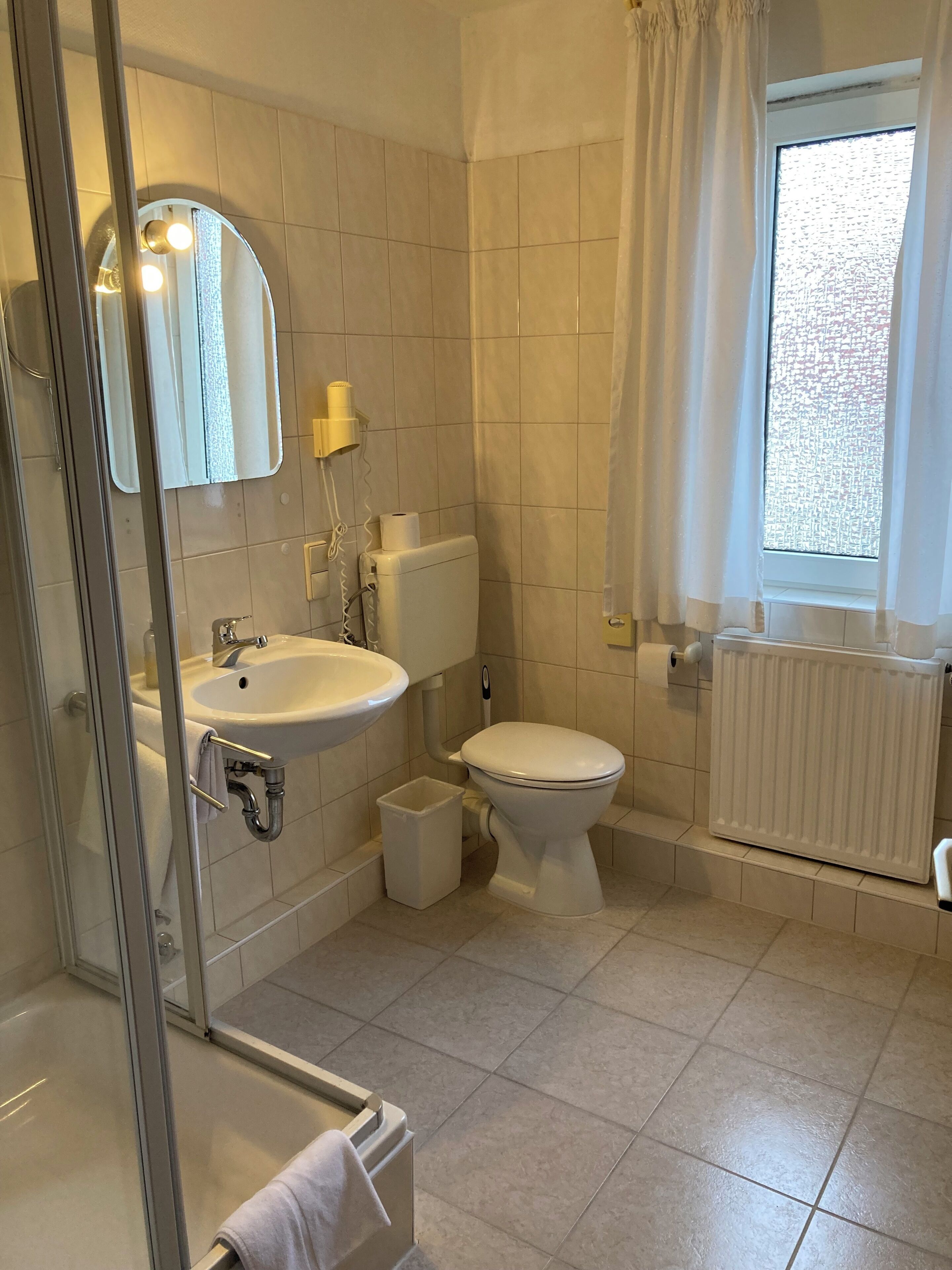 Un bagno con box doccia in vetro, lavandino, servizi igienici e una finestra con tende.
