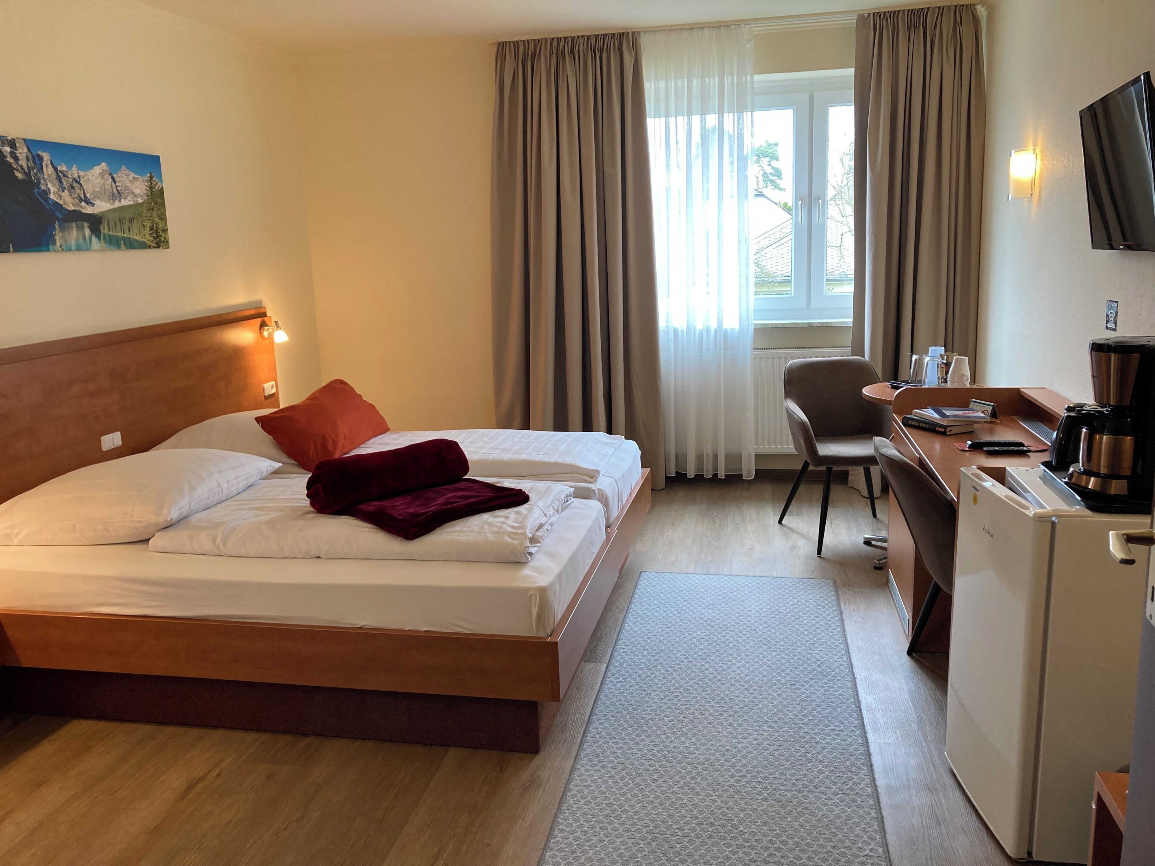 Una camera d'albergo con un letto, una scrivania con computer, una macchina del caffè e una televisione.