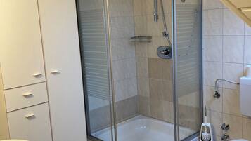 Un baño moderno con ducha de vidrio, inodoro blanco, lavamanos y un mueble con cajones.