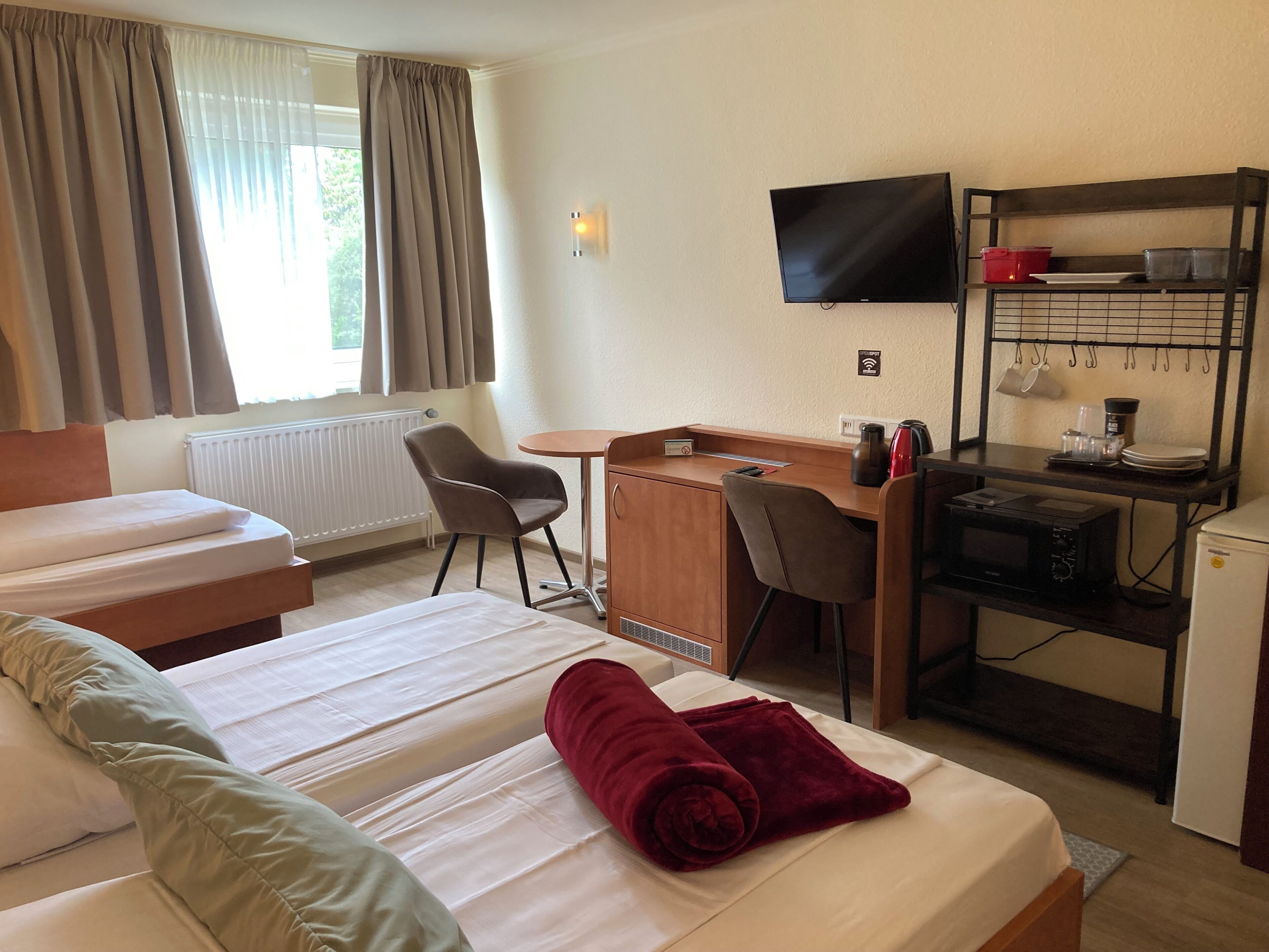 A hotel room with a bed, a desk, a chair, a television, and a kitchenette.