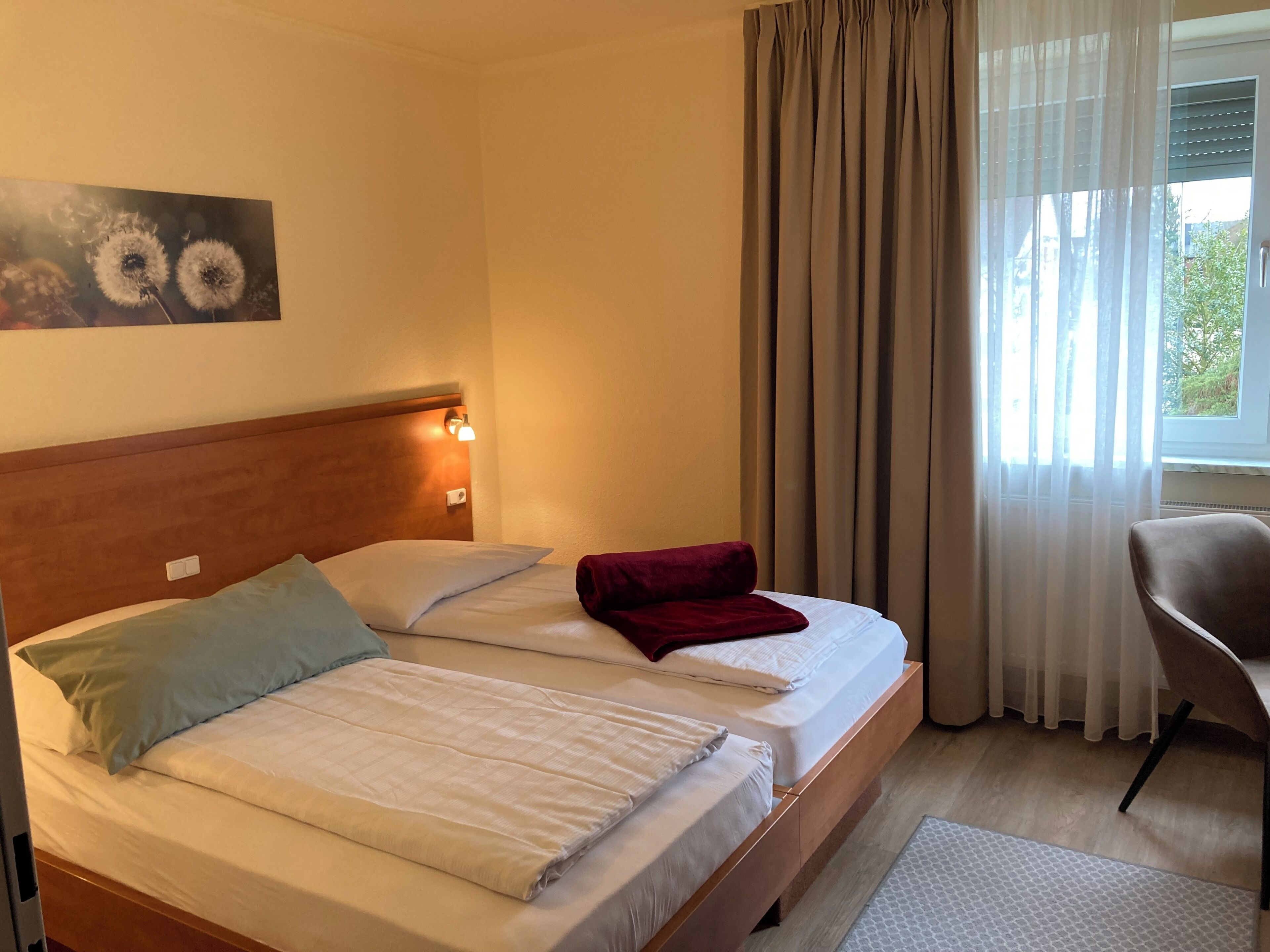 A hotel room with two beds, a headboard with a light fixture, a chair, and a window with curtains.