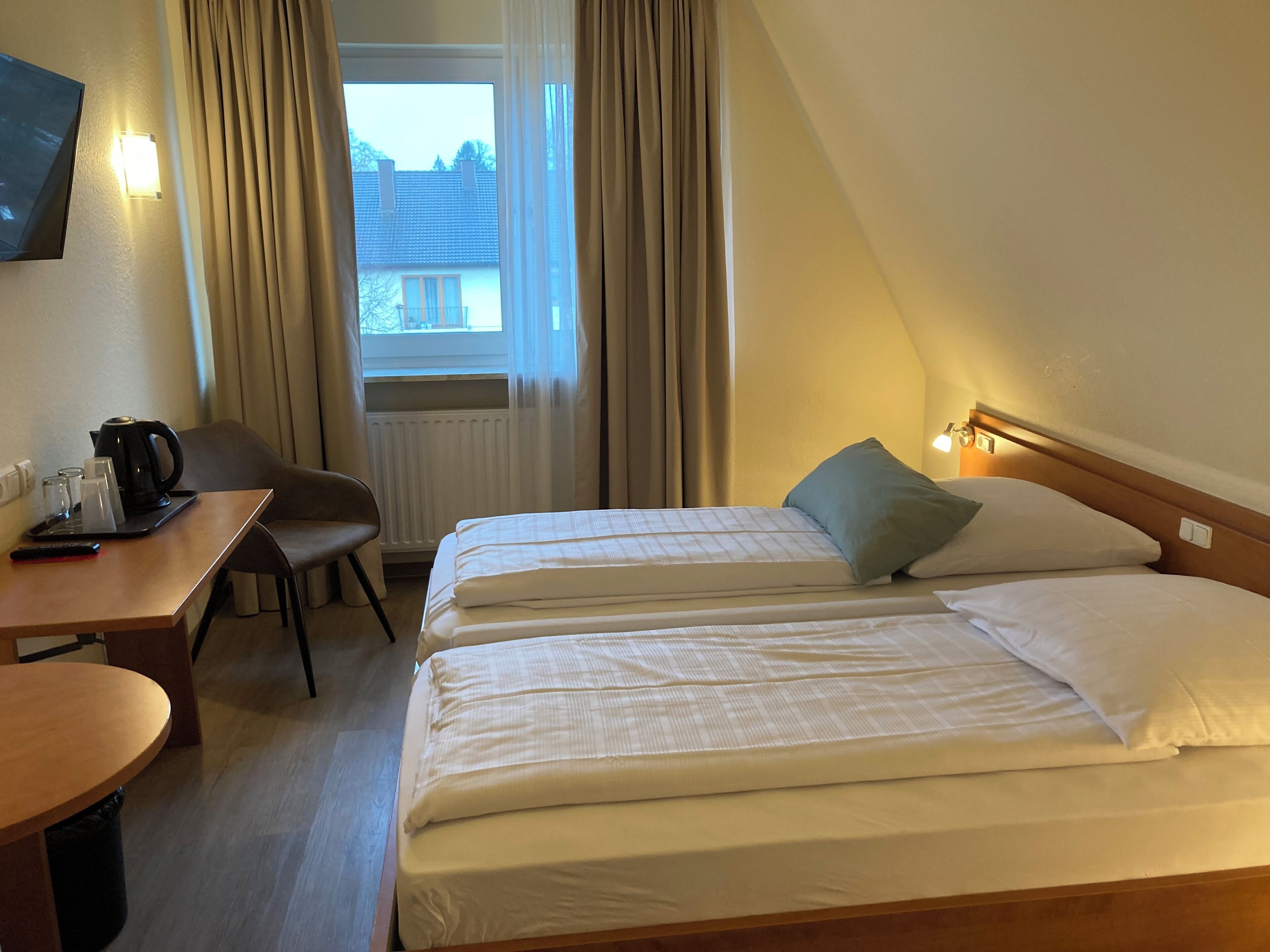A hotel room with two beds, a desk, a chair, a coffee maker, and a TV.