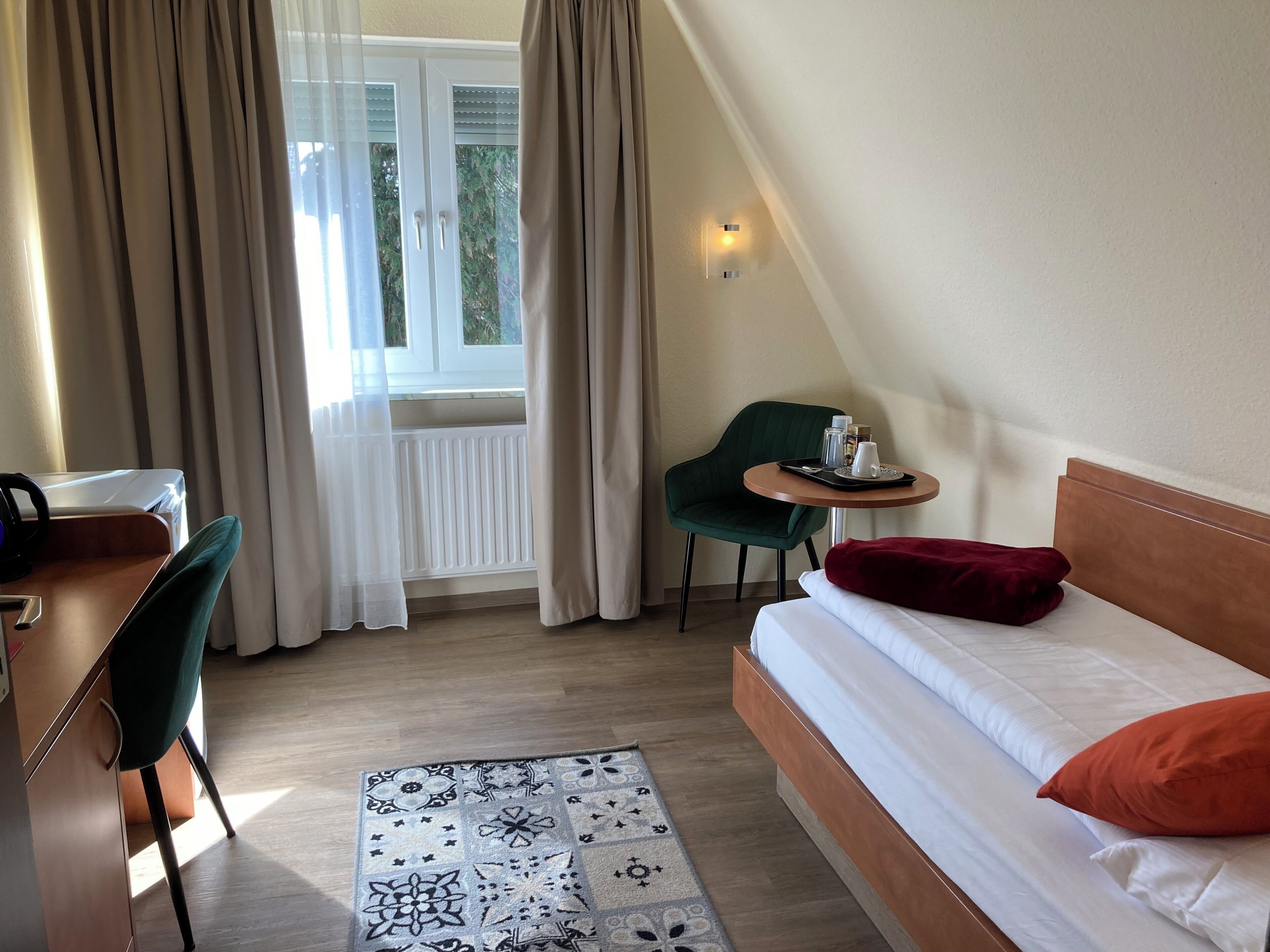 A hotel room with a bed, a desk, a chair, a small table with a tray, and a window with curtains.