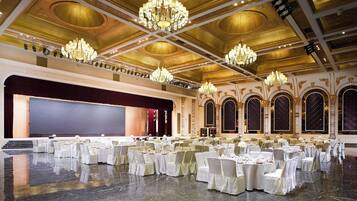 A banquet hall with a stage, chandeliers, and rows of tables set for a formal event.