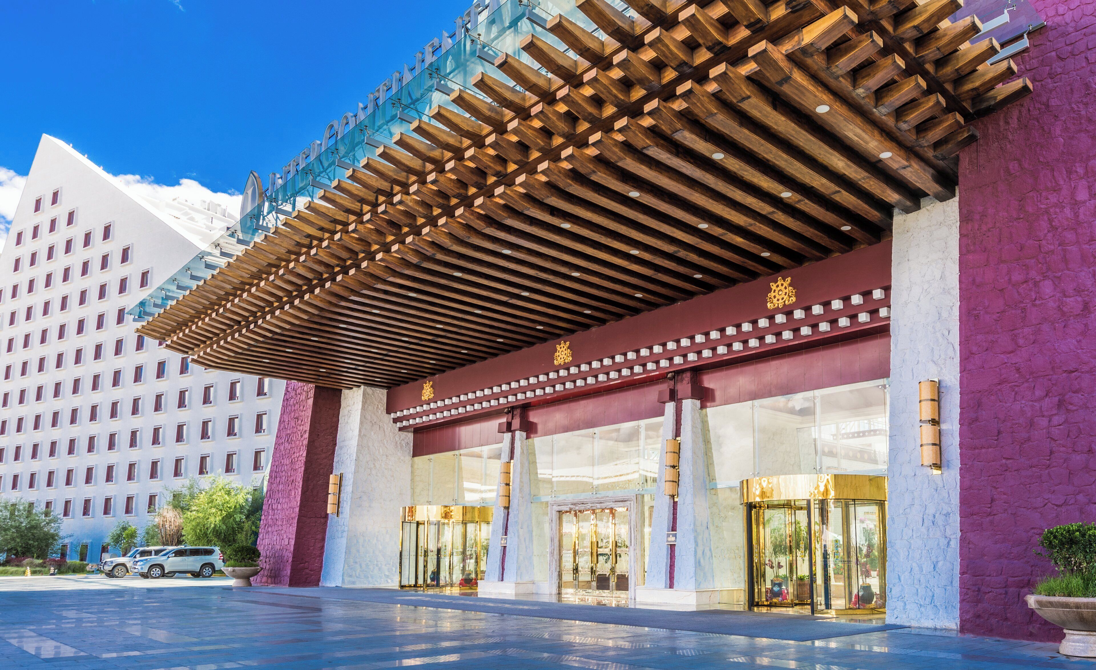 A hotel entrance with a covered entrance, large glass doors, and a parking area with a car.