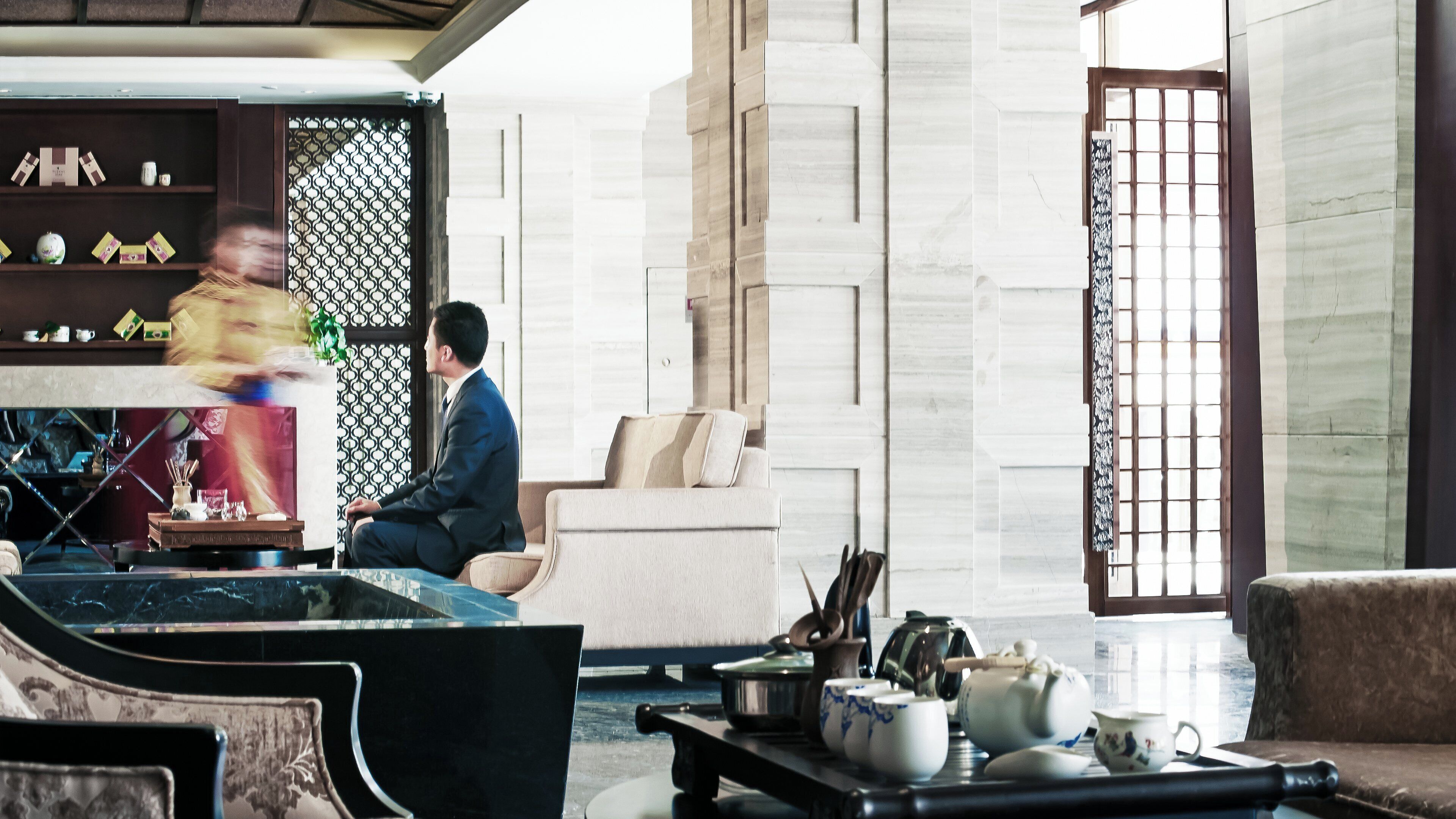 Un intérieur moderne avec un canapé, une table basse sur laquelle sont posées des théières, et un mur orné d’un motif.