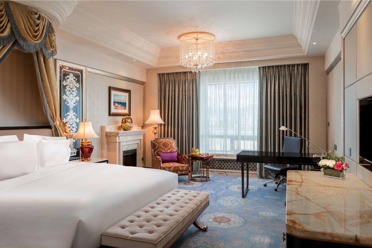 Quarto de hotel com uma cama grande, escrivaninha, cadeira, lareira e um candelabro.