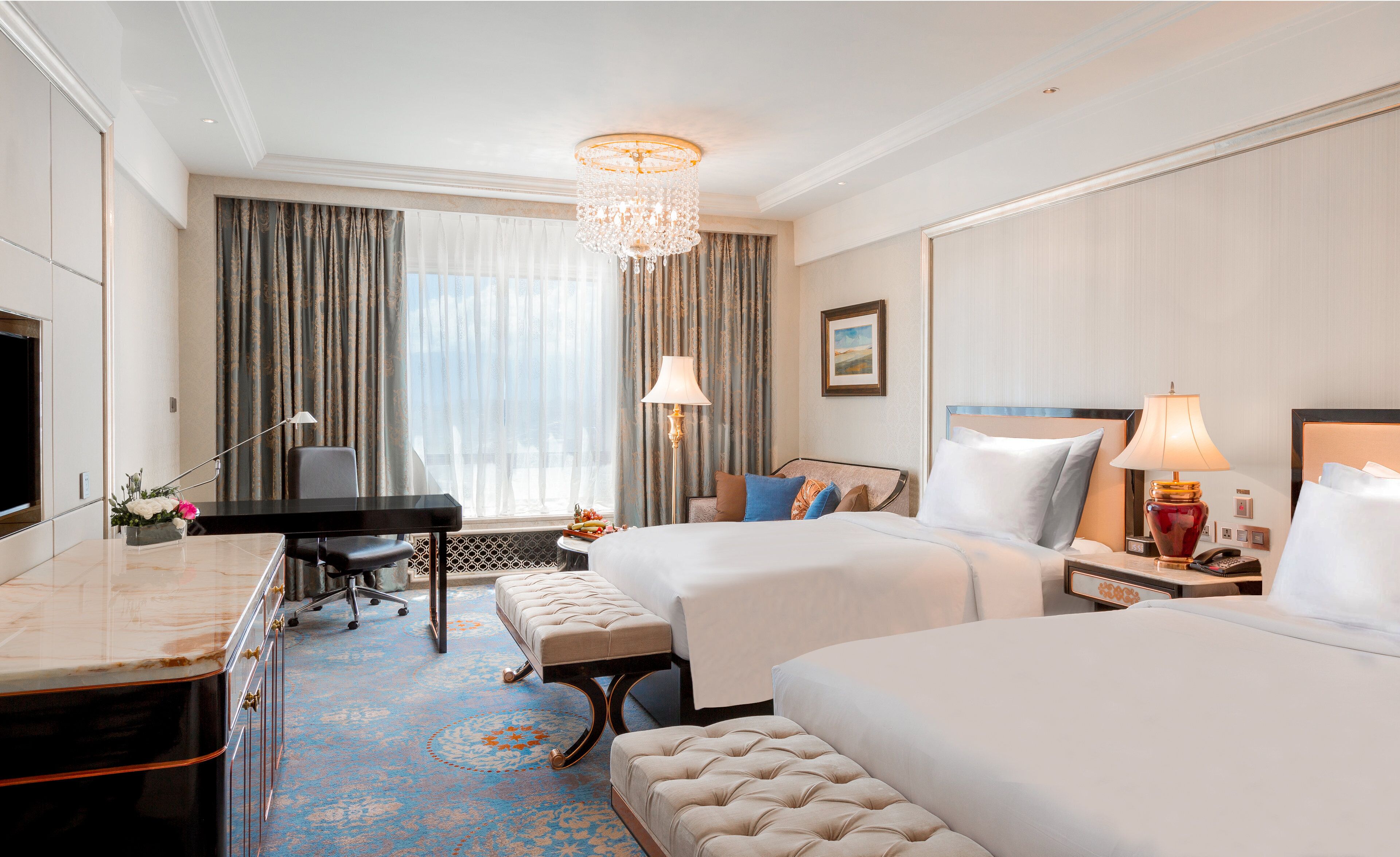 A hotel room with a bed, a desk, a chair, a lamp, and a television.