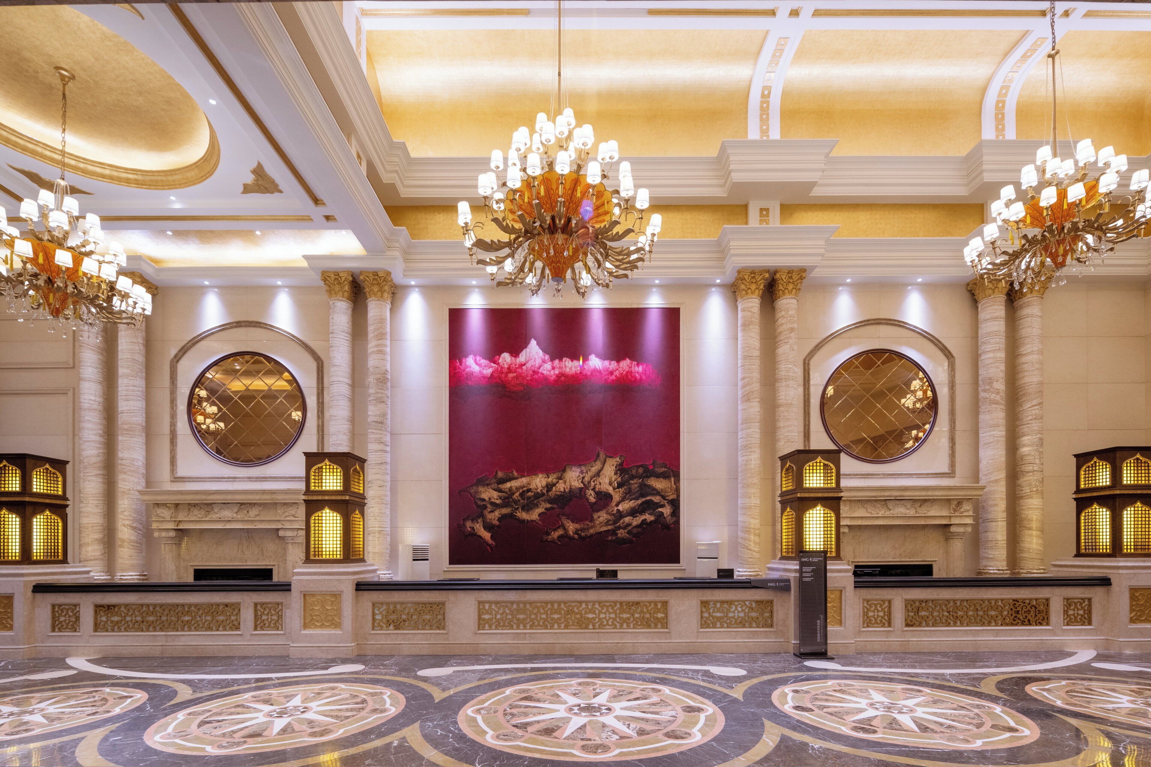 A grand lobby with ornate chandeliers, large circular mirrors, and a central artwork.