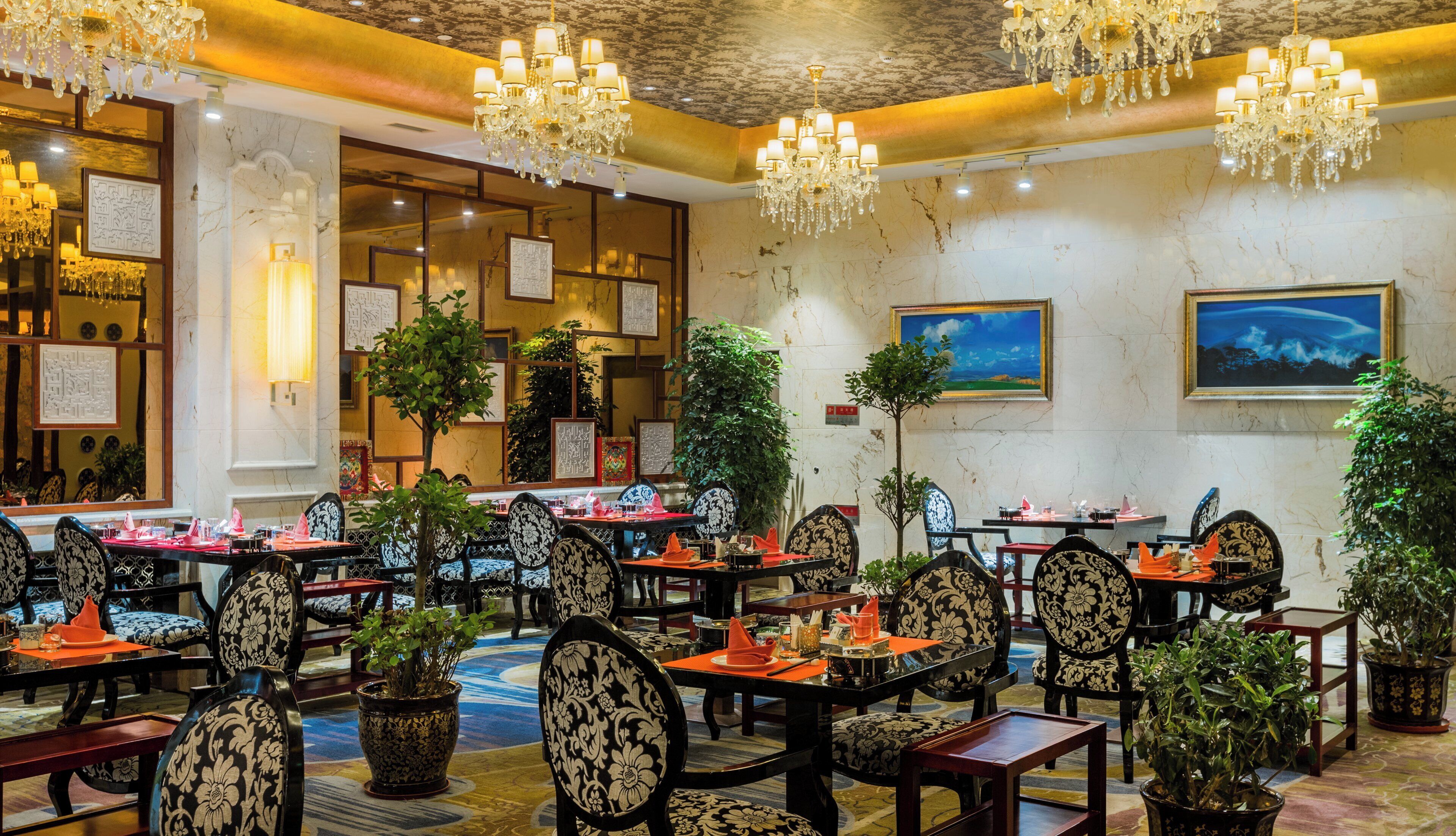 A hotel dining area with multiple tables, chairs, and chandeliers.