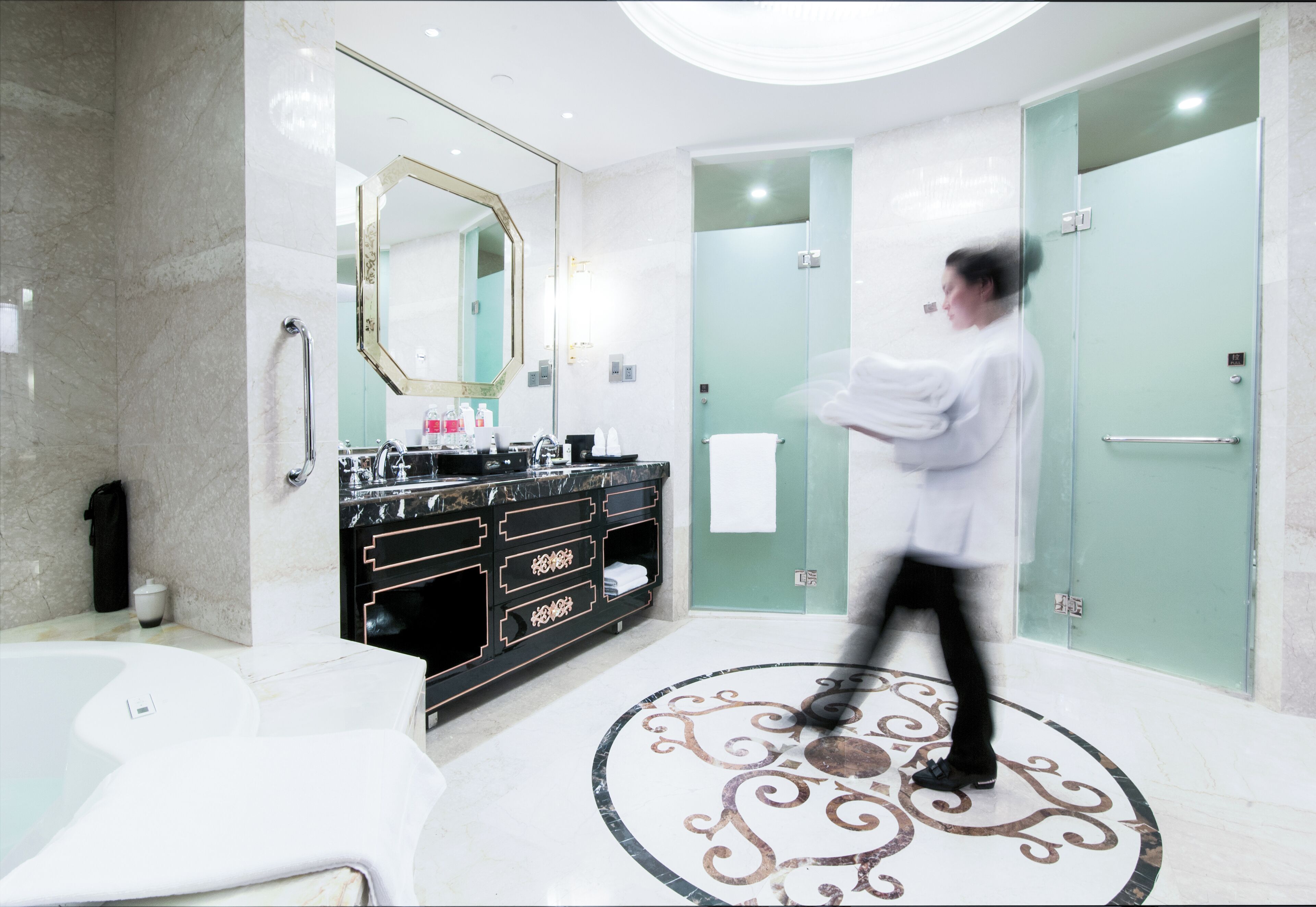 Un baño moderno con piso de mármol, un espejo grande, tocador negro y cabina de ducha con paredes de vidrio.