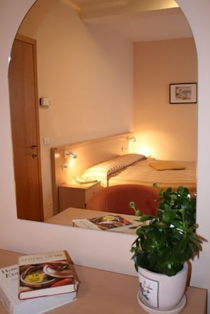 Un dormitorio con cama, mesita de noche, lámpara y una planta en maceta.