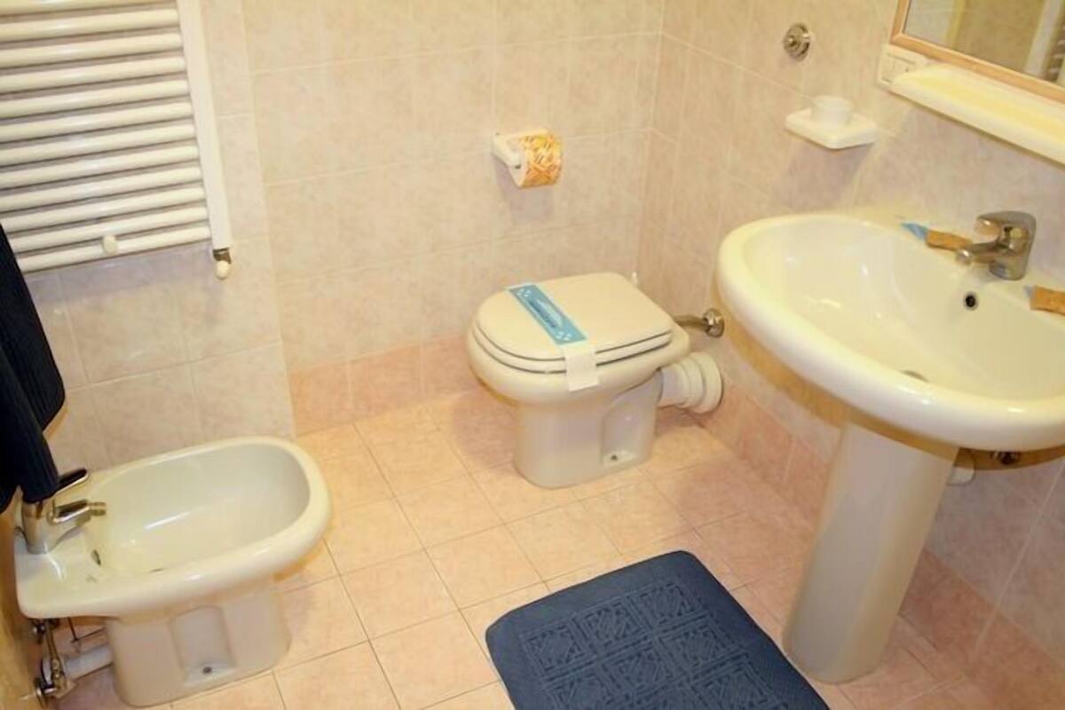 A bathroom with a bidet, toilet, sink, and a mirror.