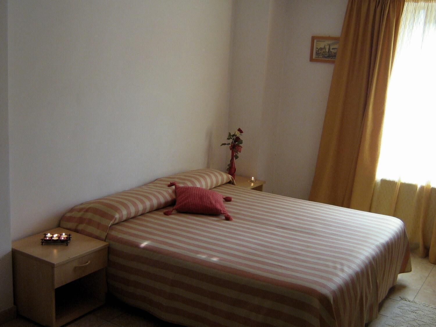 Ein Schlafzimmer mit einem Bett, einem Nachttisch, einer Vase mit Blumen und einem Bild an der Wand.