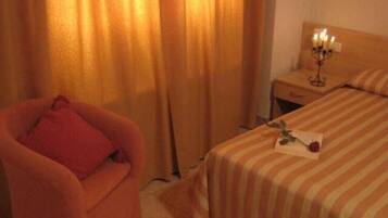 Una habitación de hotel con una cama a rayas, una silla con un cojín rojo y una mesita de noche con un candelabro.