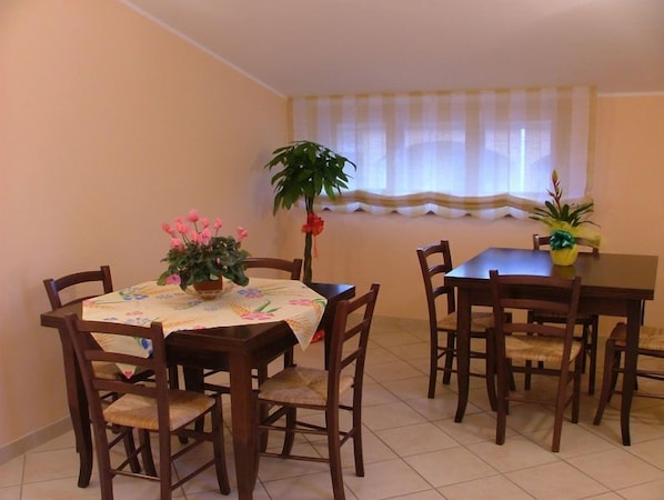 A dining area with a table set for four, surrounded by wooden chairs. There is a potted plant on the table and another on the windowsill.