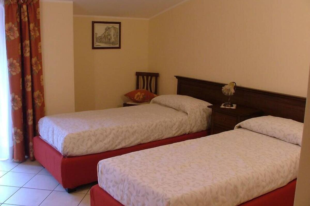 Une chambre avec deux lits simples, une tête de lit en bois, une table de chevet avec une lampe et un tableau au mur.