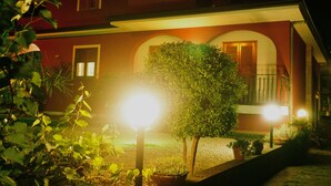 A house with a red exterior, a balcony, and a well-lit front yard with potted plants and a tree. - Casalotto Inn (Aci Sant'Antonio)