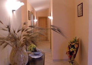 A hallway with a large potted plant, a small table with a bowl, and a framed picture on the wall.