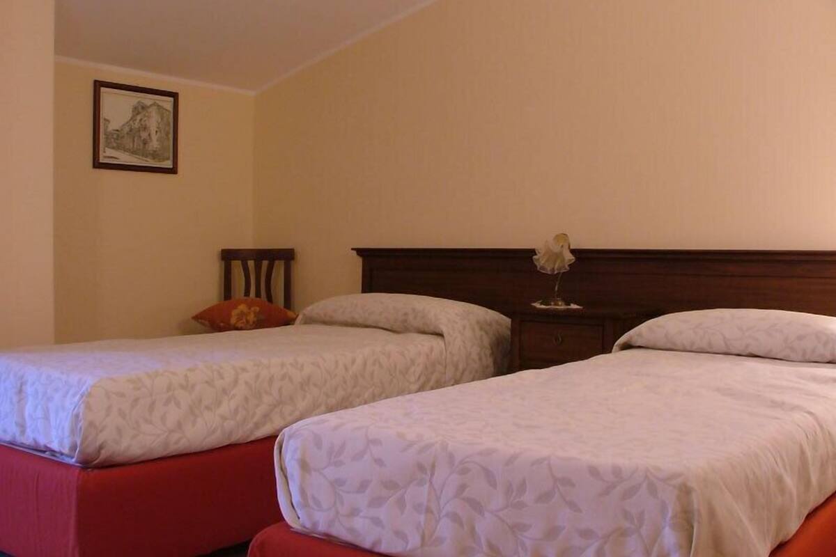 Une chambre d’hôtel avec deux lits simples, une tête de lit en bois, une petite table de chevet avec une lampe et un tableau encadré au mur.