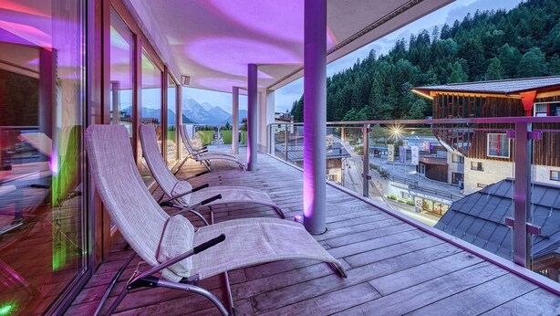Un balcón con sillones de descanso, una terraza de madera y vistas a una montaña y un bosque.