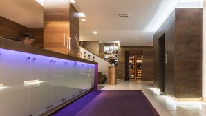 Un área de recepción moderna con un separador de vidrio, una alfombra morada y una escalera que sube a plantas superiores.