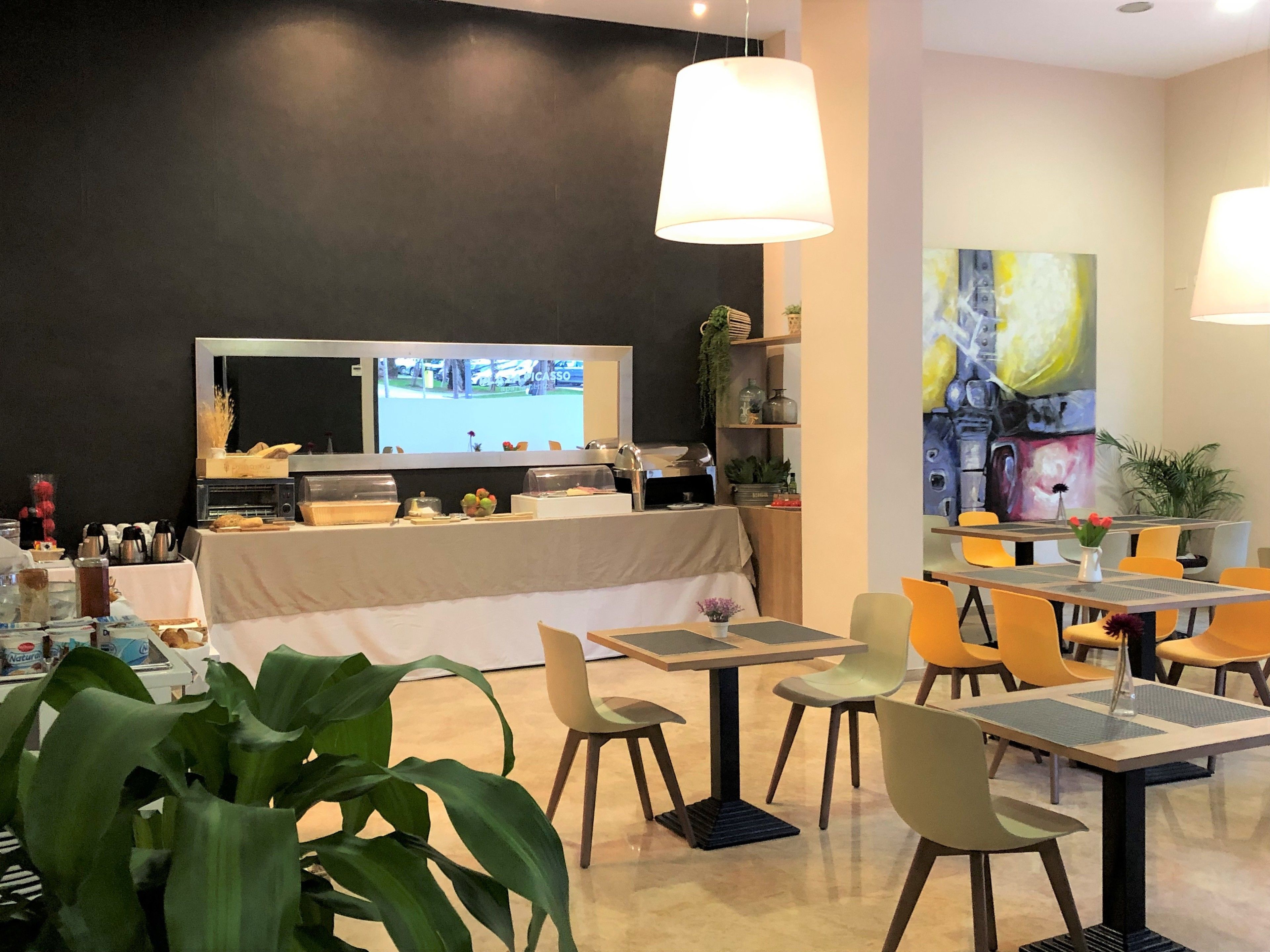 Een restaurant met een toonbank, tafels, stoelen en een groot schilderij aan de muur.