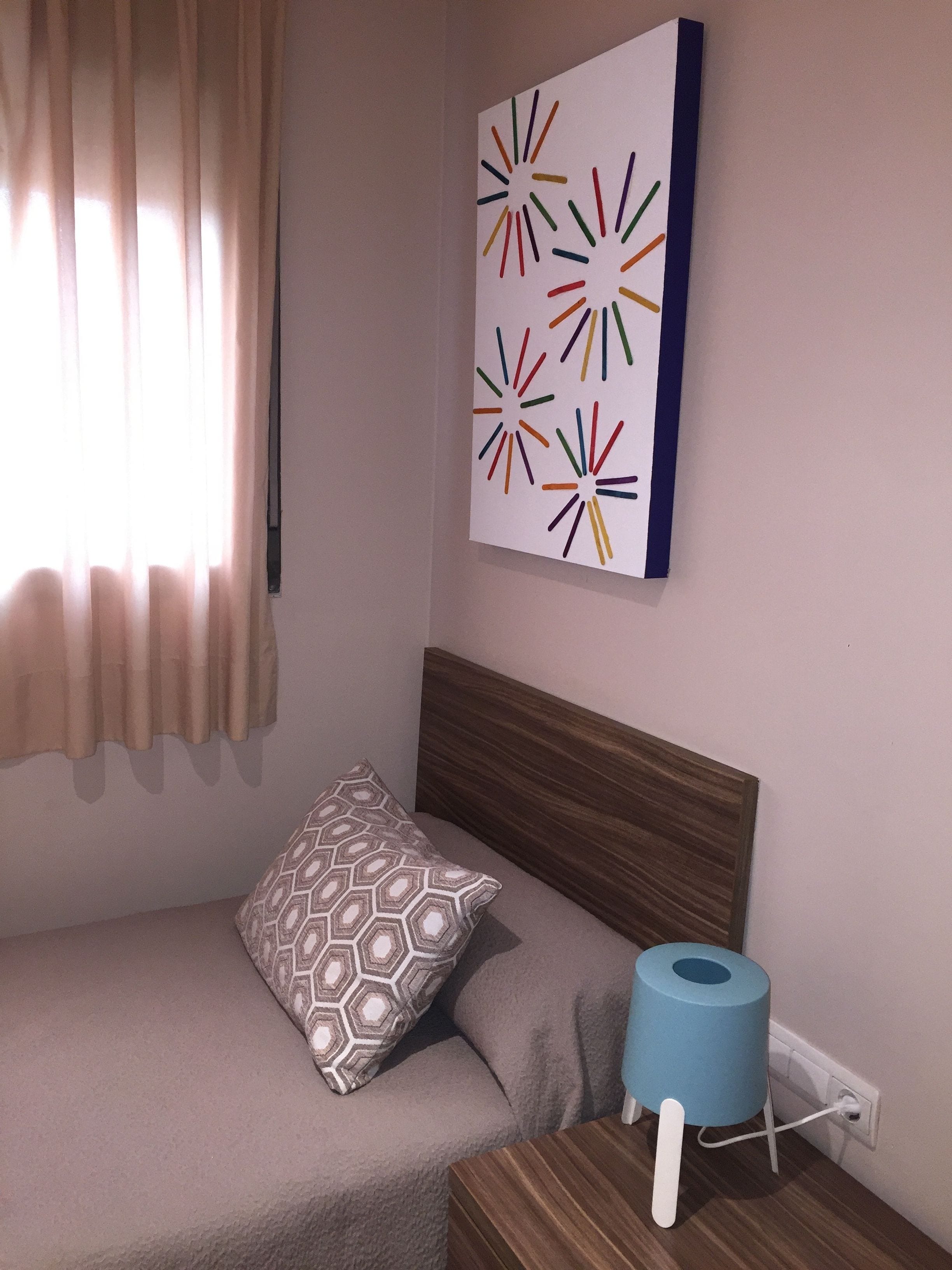 A bedroom with a bed, a patterned pillow, a wall-mounted artwork, and a blue toilet paper holder.