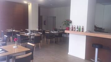 Een restaurant met verschillende tafels en stoelen, een bar met krukken, en een kamerplant.