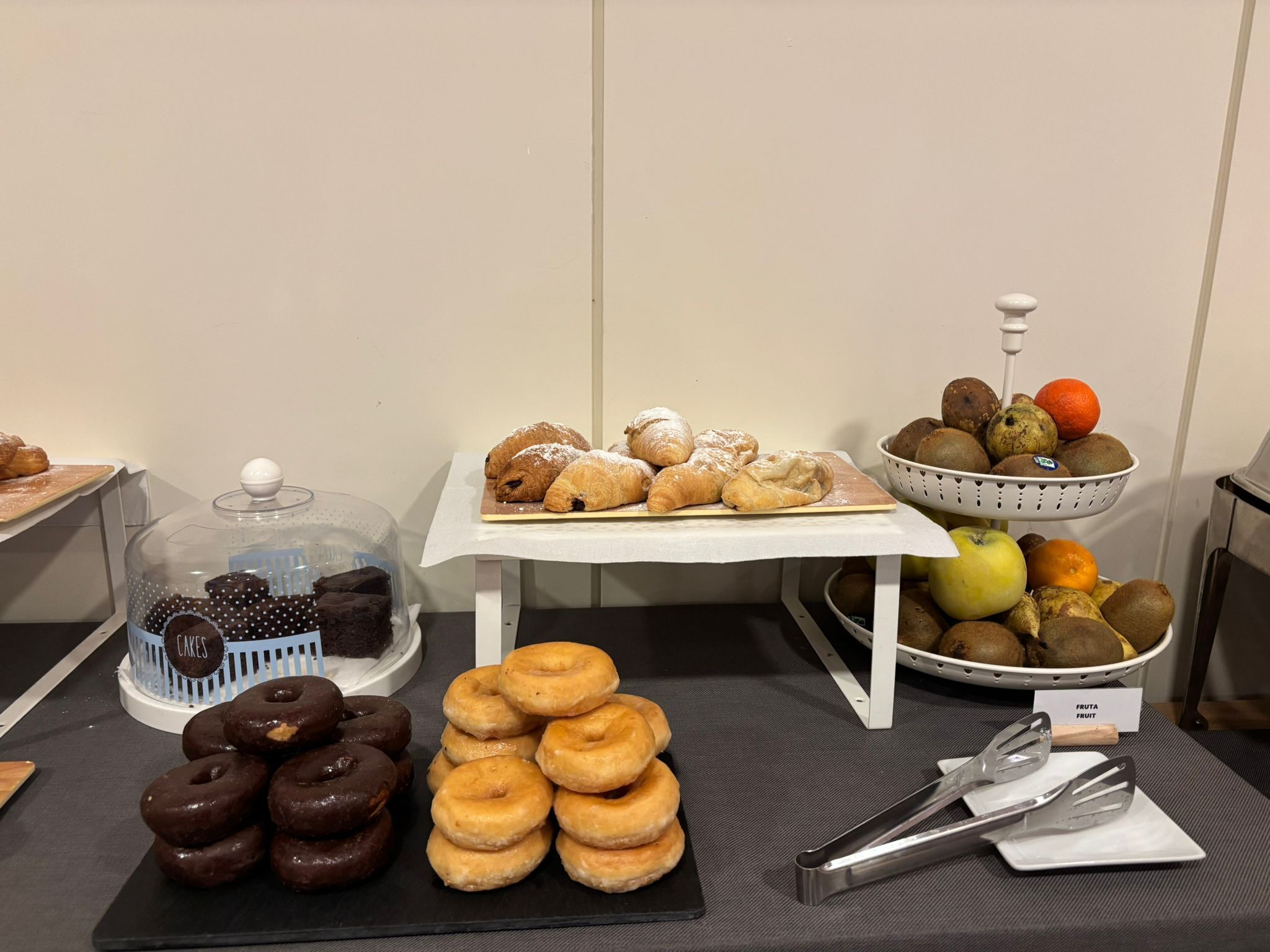 A buffet table with various baked goods, including pastries and donuts, and a fruit bowl.