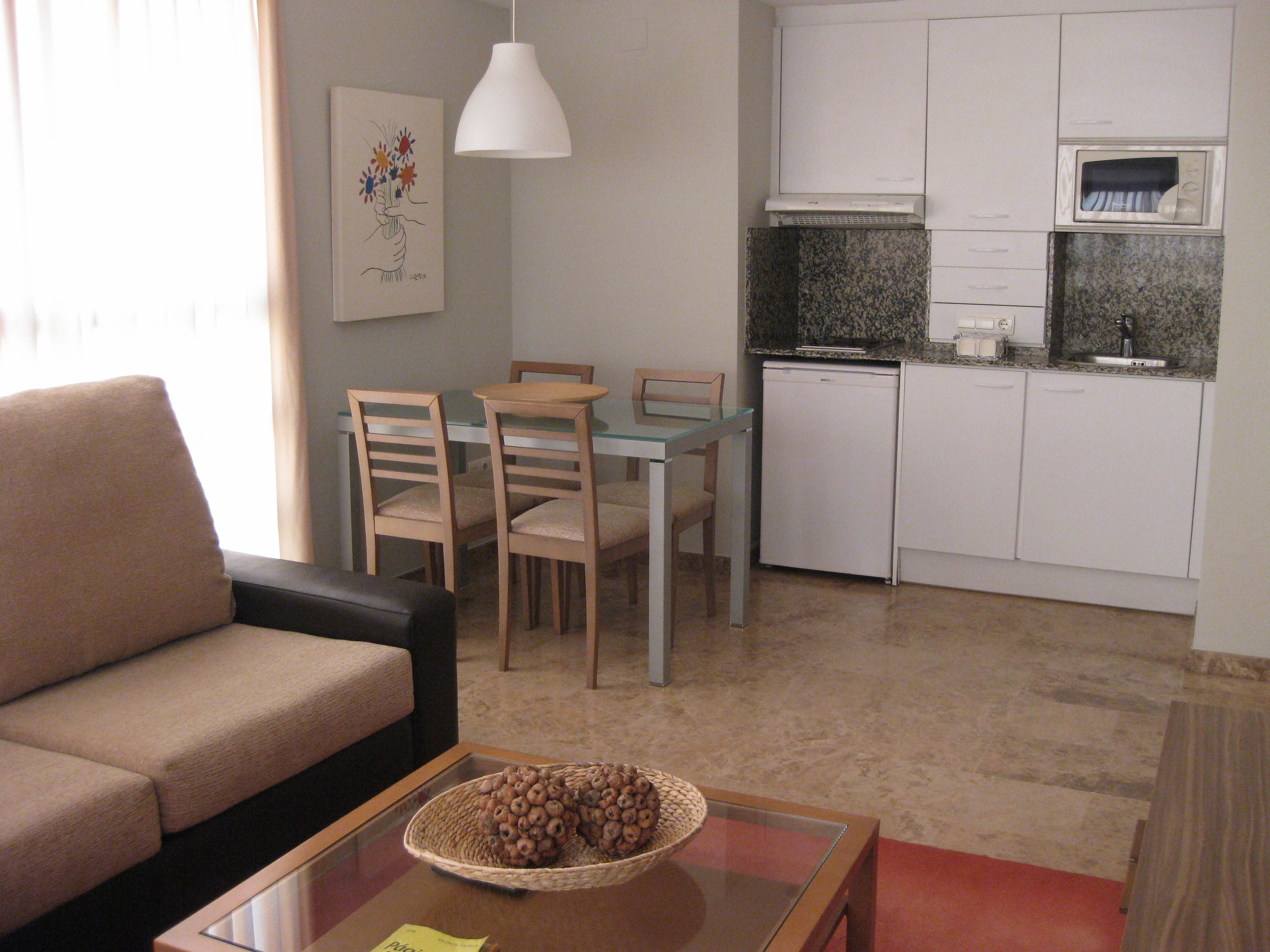 Un espace de vie compact comprenant un canapé, une table à manger, des chaises, un coin cuisine avec un four à micro-ondes et un élément décoratif mural.