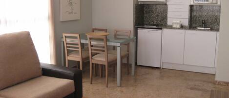 A compact living space with a sofa, dining table, chairs, a kitchen area with a microwave, and a decorative wall piece.