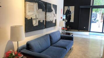 A modern lobby with a blue sofa, abstract wall art, a vase with flowers, and a lamp.