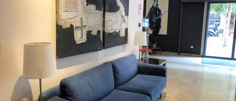 Un vestíbulo moderno con un sofá azul, arte abstracto en la pared, un jarrón con flores y una lámpara.