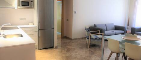 A modern kitchen with a built-in microwave, a stainless steel refrigerator, and a sink. There is a dining area with a table and chairs.
