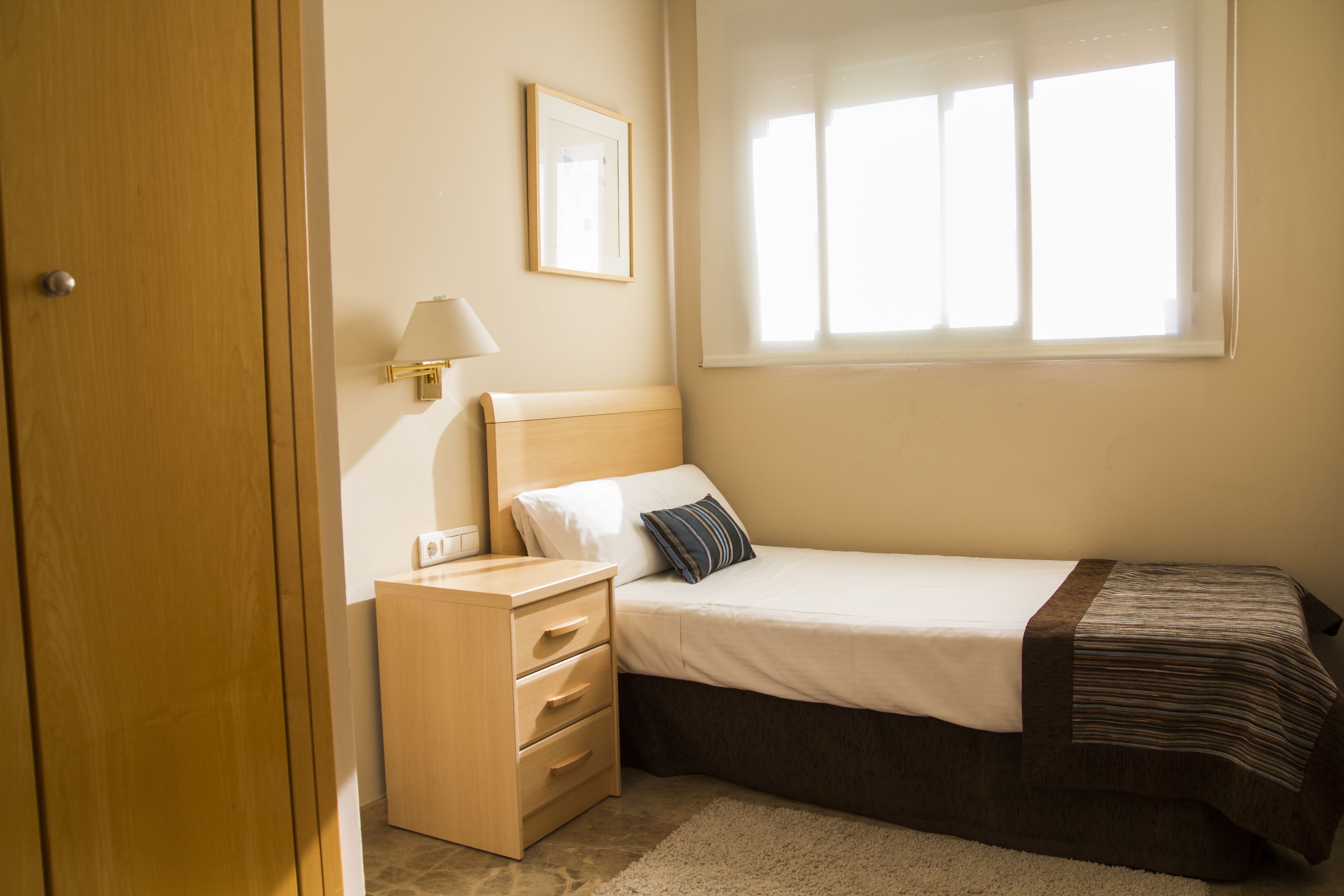 Une chambre à coucher avec un lit, une table de chevet, une lampe et une fenêtre avec des stores.
