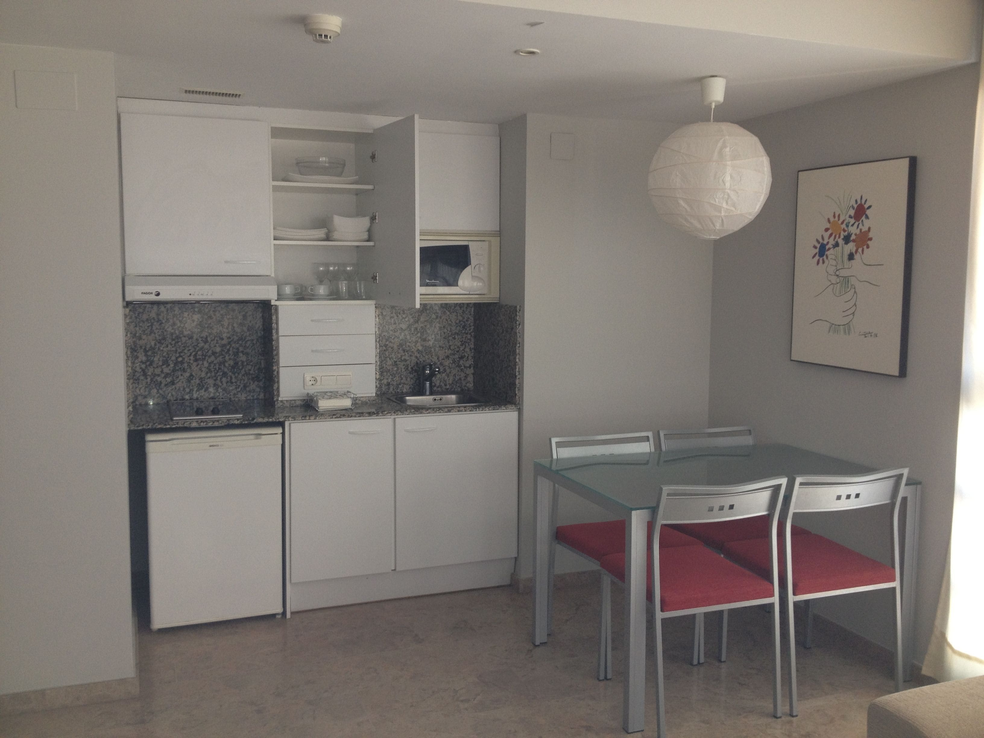 A modern kitchen with white cabinets, a granite countertop, and a dining area with a glass table and red chairs.