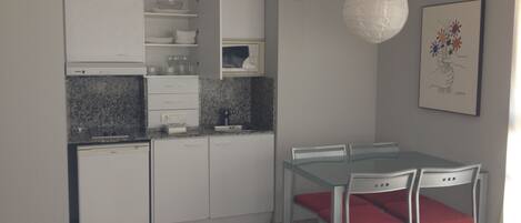 A modern kitchen with white cabinets, a granite countertop, and a dining area with a glass table and red chairs.
